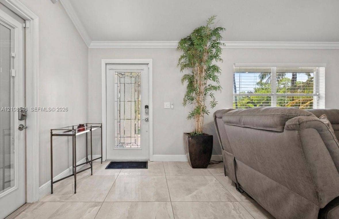 Large-format tile flooring, vaulted ceilings with crown molding, and an entry door featuring decorative glass inlay