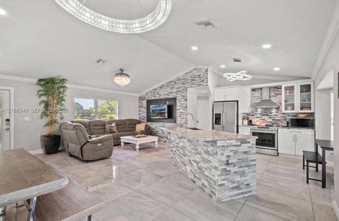 Open-concept area featuring stone-clad kitchen island, stacked stone accent wall, recessed lighting, modern geometric chandeliers, and large-format tile flooring