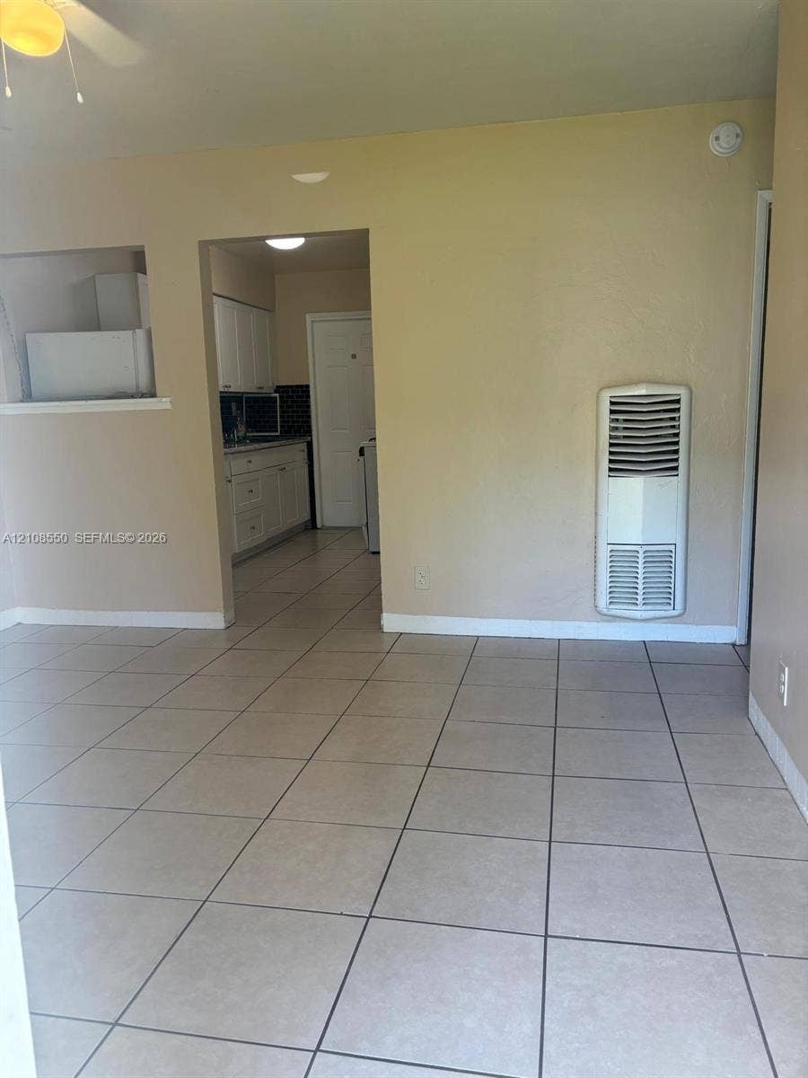 Neutral-toned tile flooring, wall-mounted heater, ceiling fan with light fixture, and kitchen cabinetry with contrast backsplash