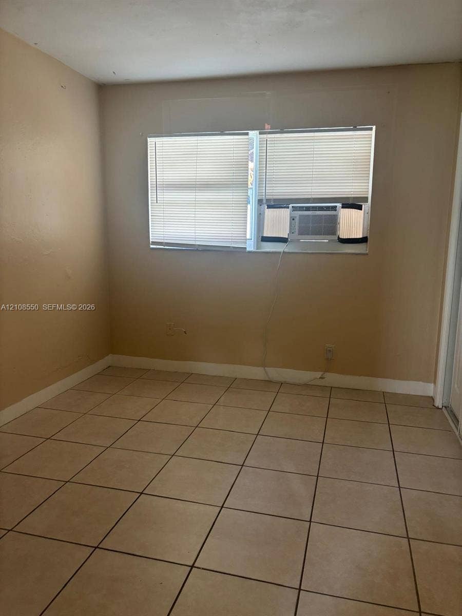 Neutral-toned interior space featuring light-colored ceramic tile flooring, a dual-pane horizontal window with integrated blinds, and painted walls