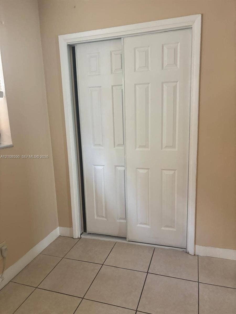 White six-panel sliding closet doors featuring smooth-finish wood casing and neutral ceramic tile flooring