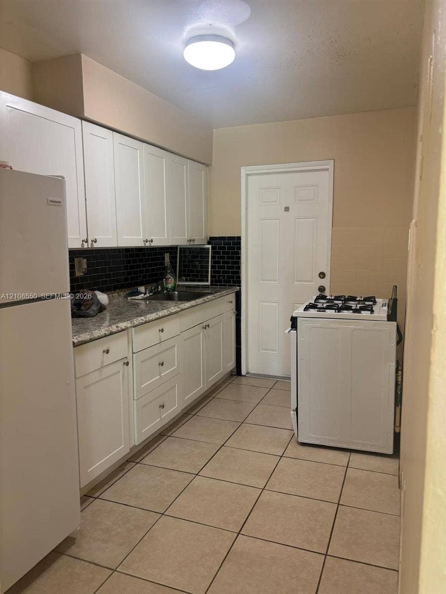 Kitchen featuring white shaker-style cabinetry, stone-finish countertops, black subway tile backsplash, and tile flooring