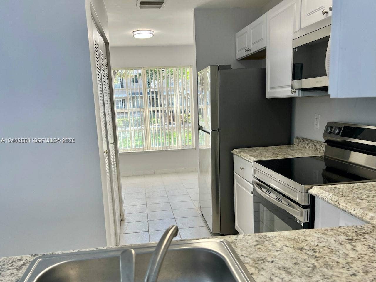 Kitchen featuring stone-finish countertops, stainless steel appliances, white cabinetry, a double-basin stainless steel sink, and ceramic tile flooring