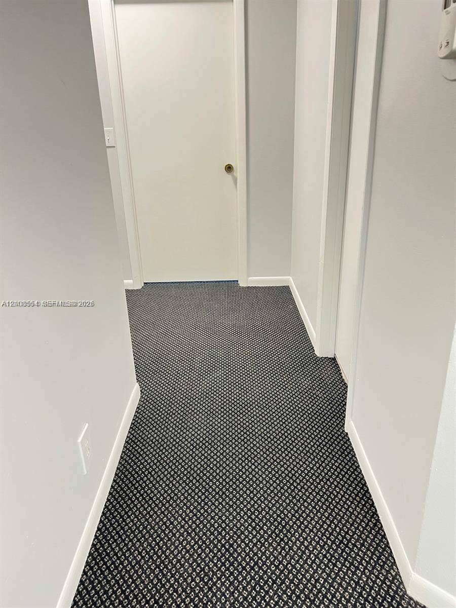Hallway featuring neutral wall paint, geometric patterned carpeting, and a solid-core interior door with a brushed metal handle