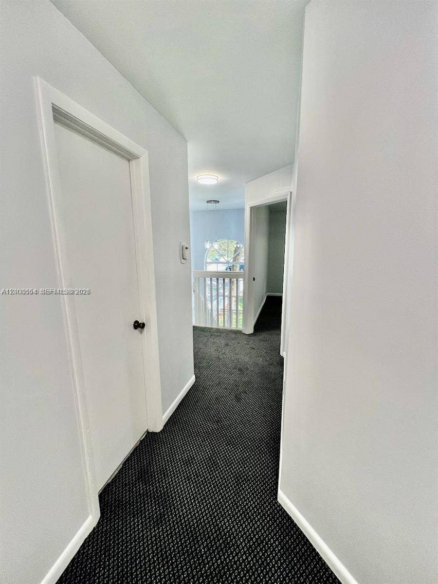 Hallway featuring dark carpeting, white interior doors, and a white baluster railing