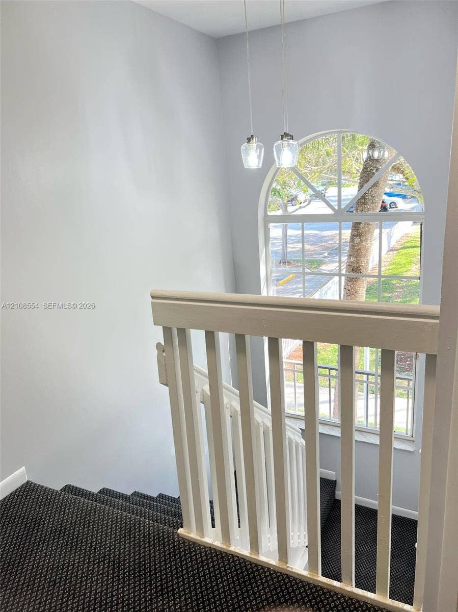 Stairwell featuring white wooden balusters, an arched window with muntin detailing, and dual pendant light fixtures