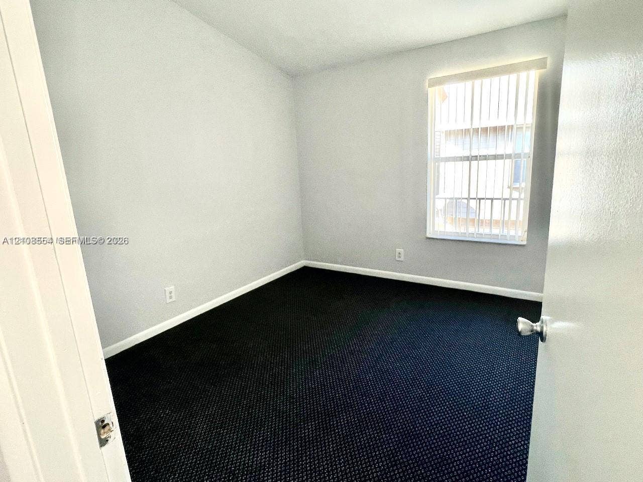 Neutral wall palette, dark carpeting, and a window with vertical blinds