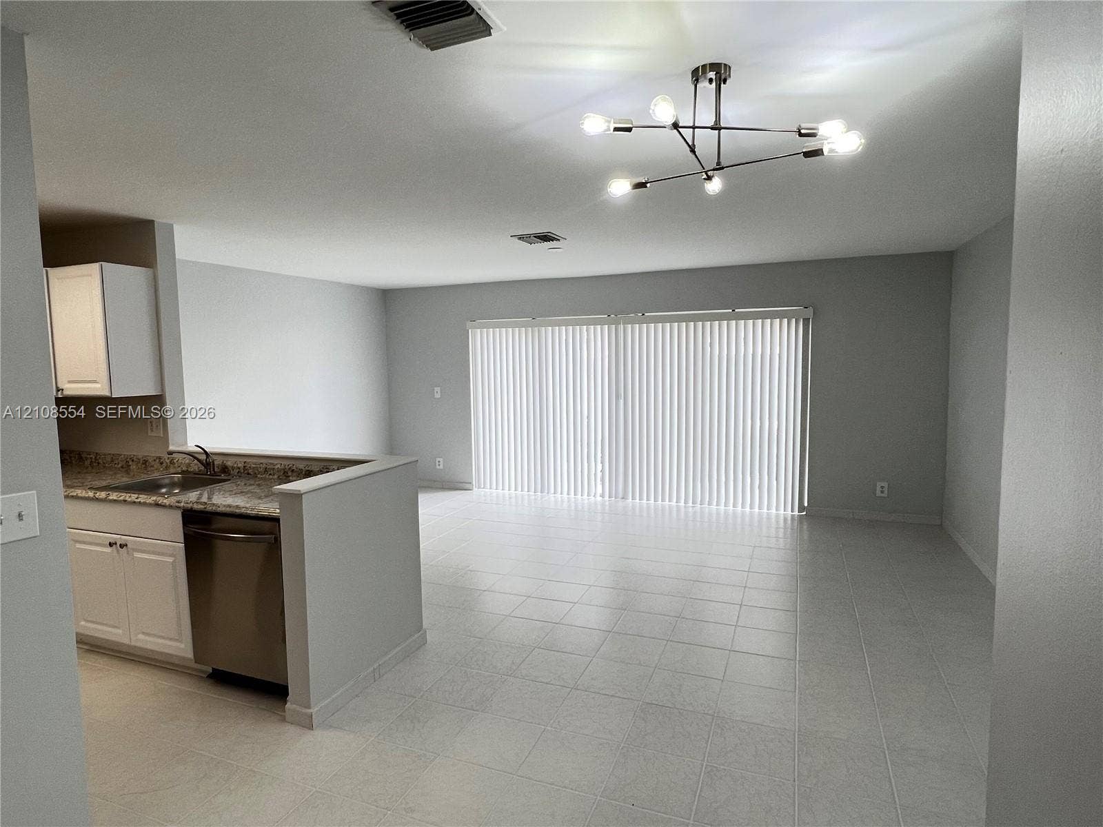 Kitchen featuring white cabinetry, stone-surface countertops, and a stainless steel dishwasher, accented by tile flooring and a multi-arm geometric light fixture
