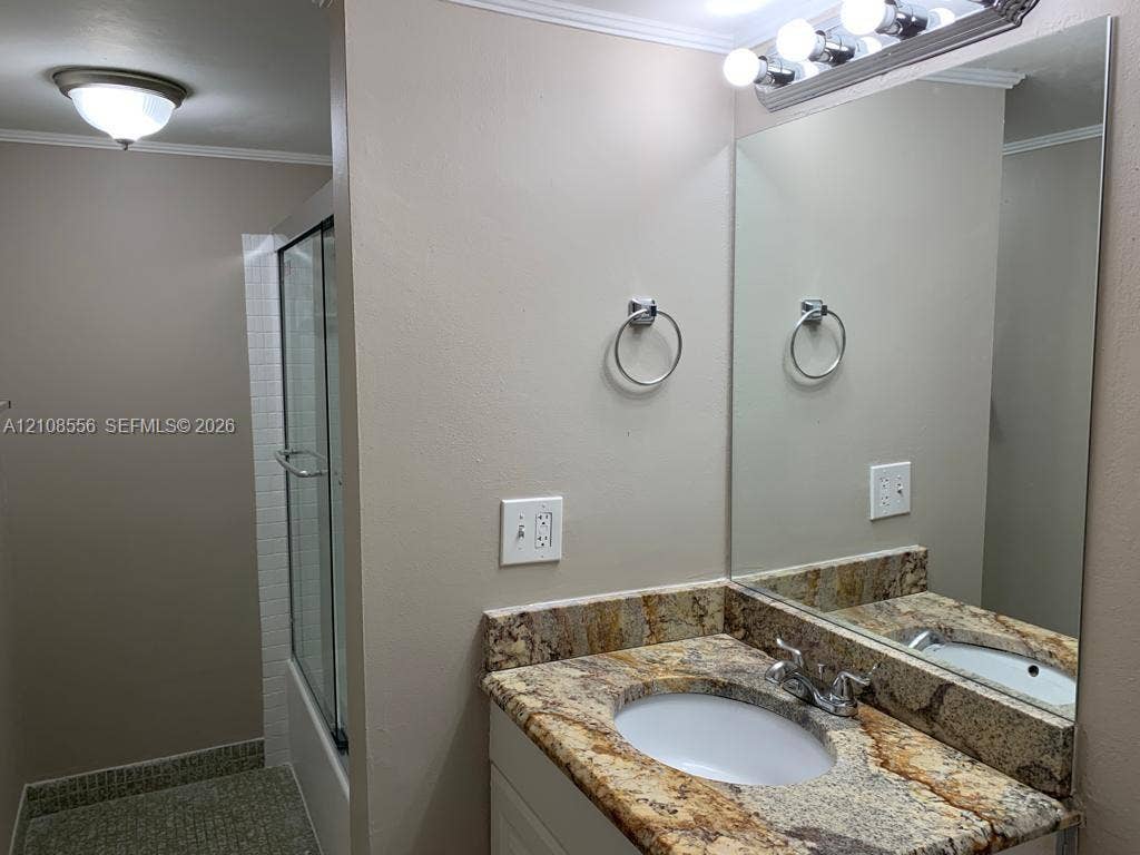 600 SW 2nd Avenue, #137, Boca Raton, FL 33432 Vanity featuring stone countertop with integrated sink, full-width wall mirror, four-light vanity fixture, and enclosed glass shower