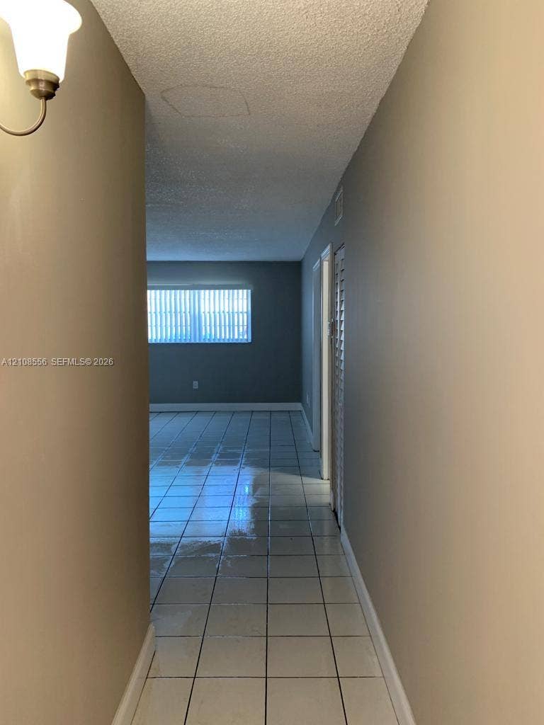600 SW 2nd Avenue, #137, Boca Raton, FL 33432 Hallway featuring tile flooring, neutral wall paint, a wall-mounted light fixture, and louvered closet doors