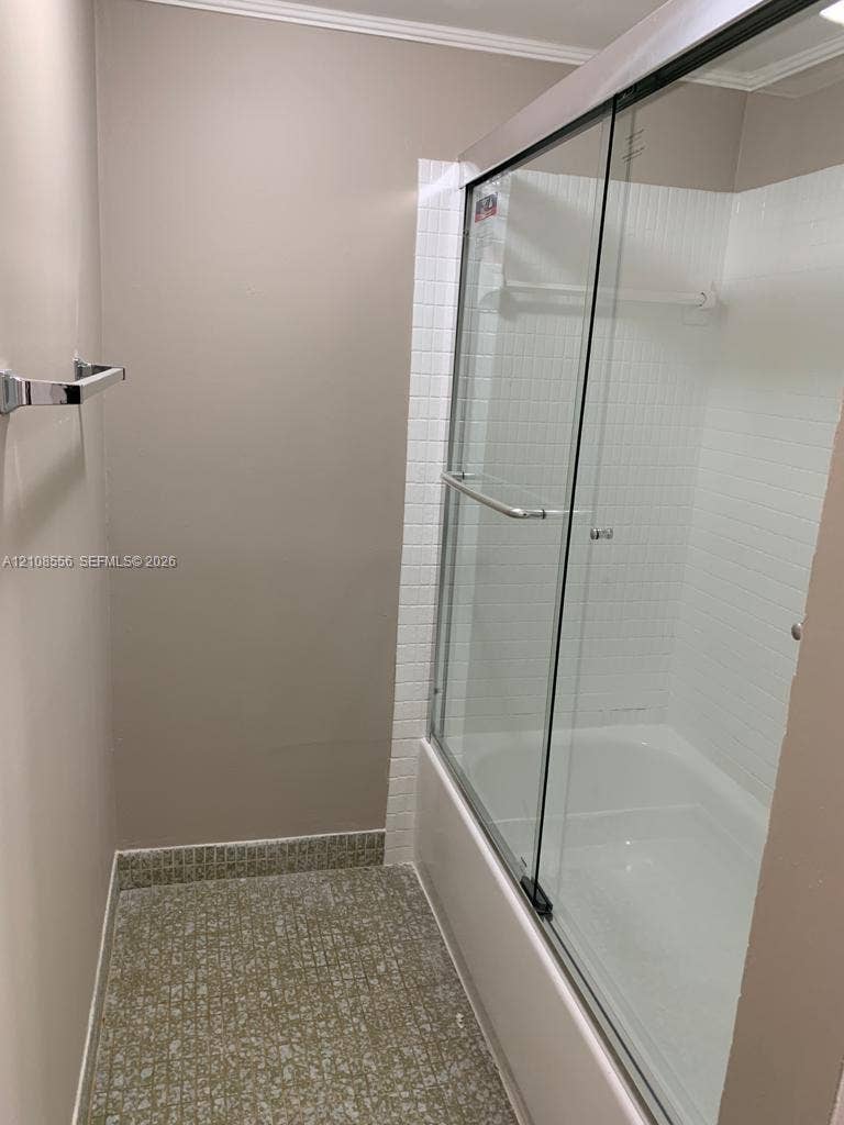 600 SW 2nd Avenue, #137, Boca Raton, FL 33432 Tub and shower combination featuring a glass sliding enclosure, white tiled surround, chrome fixtures, and patterned flooring