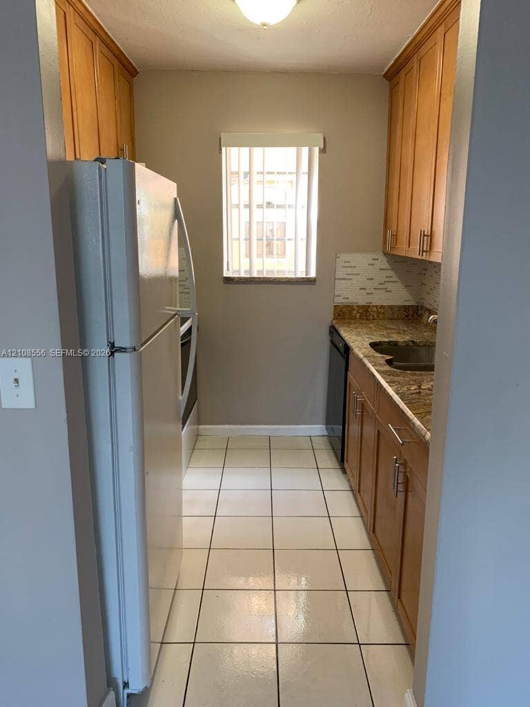 600 SW 2nd Avenue, #137, Boca Raton, FL 33432 Kitchen featuring natural wood cabinetry, stone countertops, tiled backsplash, large-format tile flooring, and a window