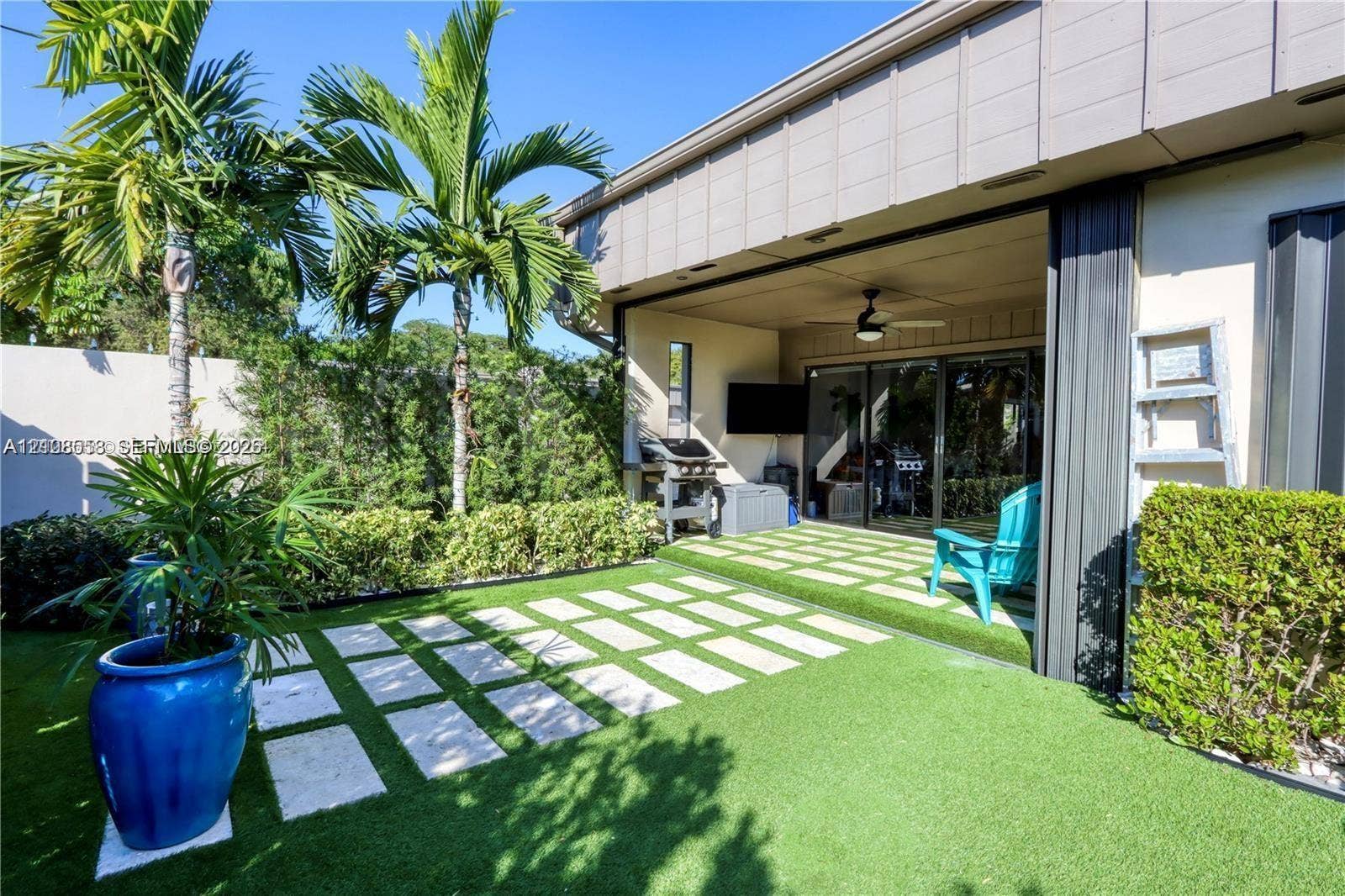 10478 SW 75th Lane, #10478, Miami, Miami, FL 33173 Outdoor patio featuring synthetic turf, light-toned stone pavers, a covered ceiling with an integrated fan, and lush perimeter landscaping