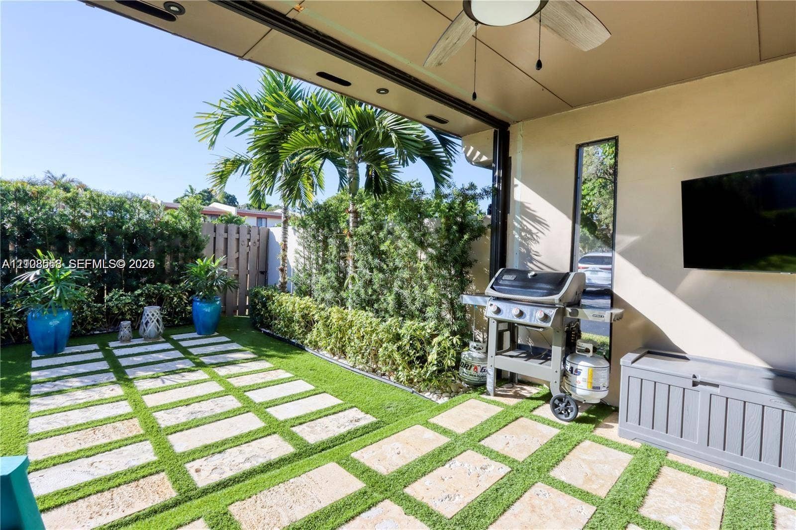 10478 SW 75th Lane, #10478, Miami, Miami, FL 33173 Covered patio with recessed lighting and a ceiling fan, featuring stone pavers with inset synthetic turf, privacy fencing, and perimeter landscaping