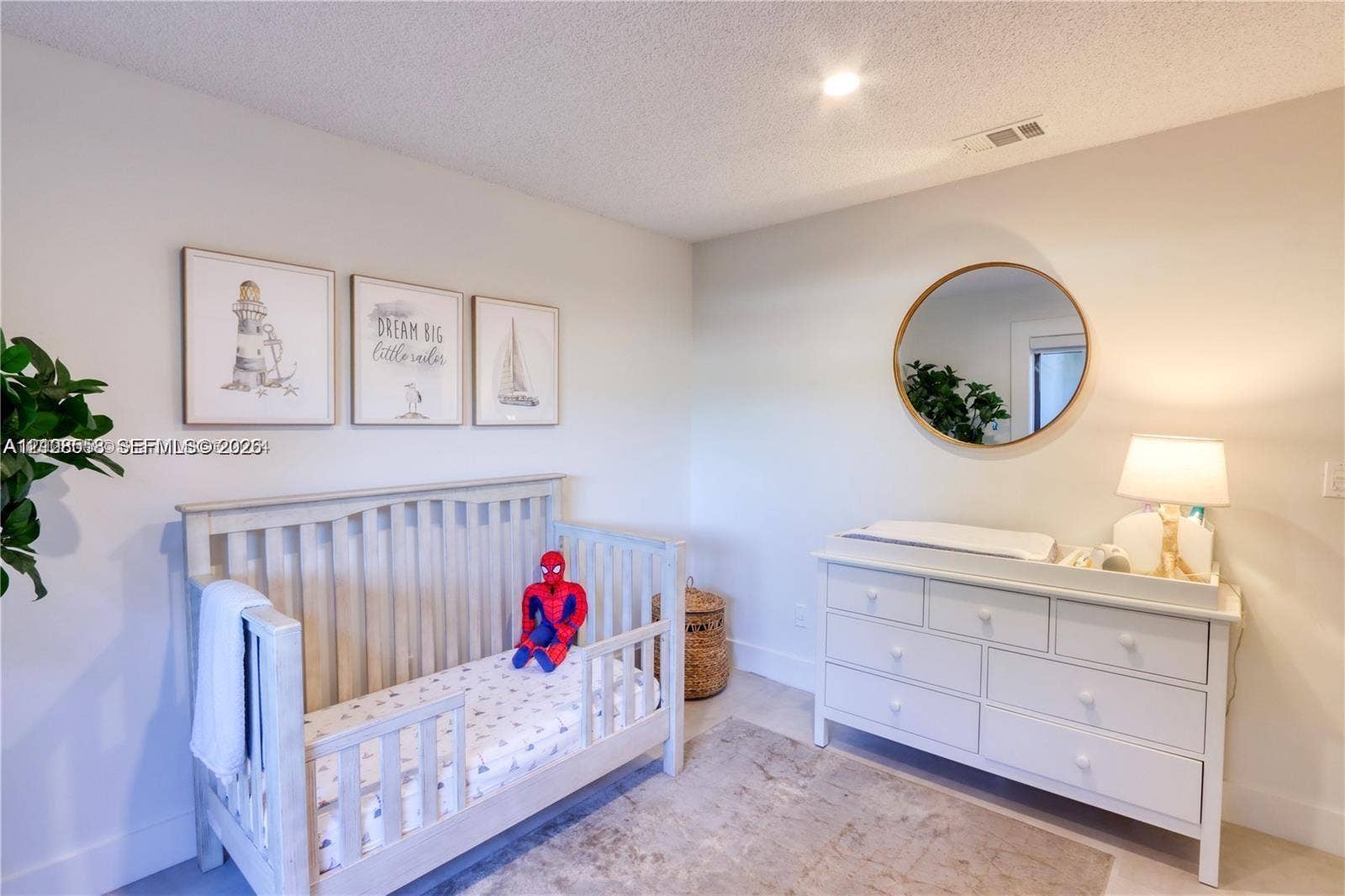 10478 SW 75th Lane, #10478, Miami, Miami, FL 33173 Neutral-toned interior space featuring a circular wall mirror with a metallic frame, textured ceiling, and uniform wall finishes