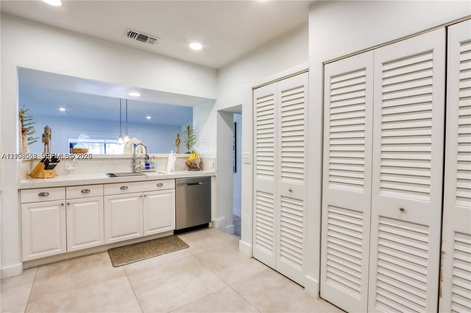 10478 SW 75th Lane, #10478, Miami, Miami, FL 33173 White cabinetry with metal hardware, light-colored solid surface countertops, stainless steel dishwasher, and floor-to-ceiling louvered closet doors