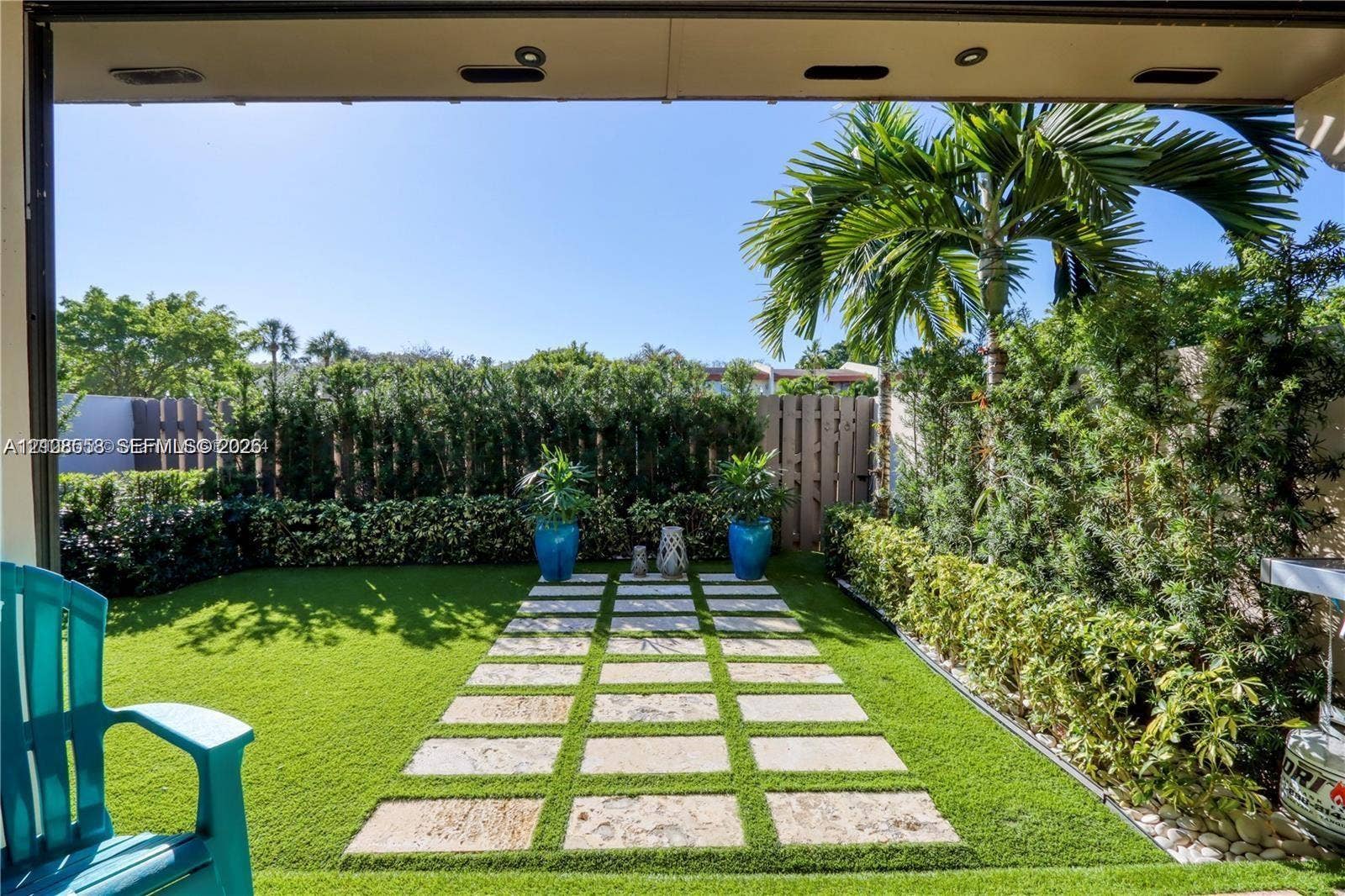 10478 SW 75th Lane, #10478, Miami, Miami, FL 33173 Enclosed backyard featuring synthetic turf, stone paver pathway, mature perimeter hedge privacy screen, and recessed soffit lighting