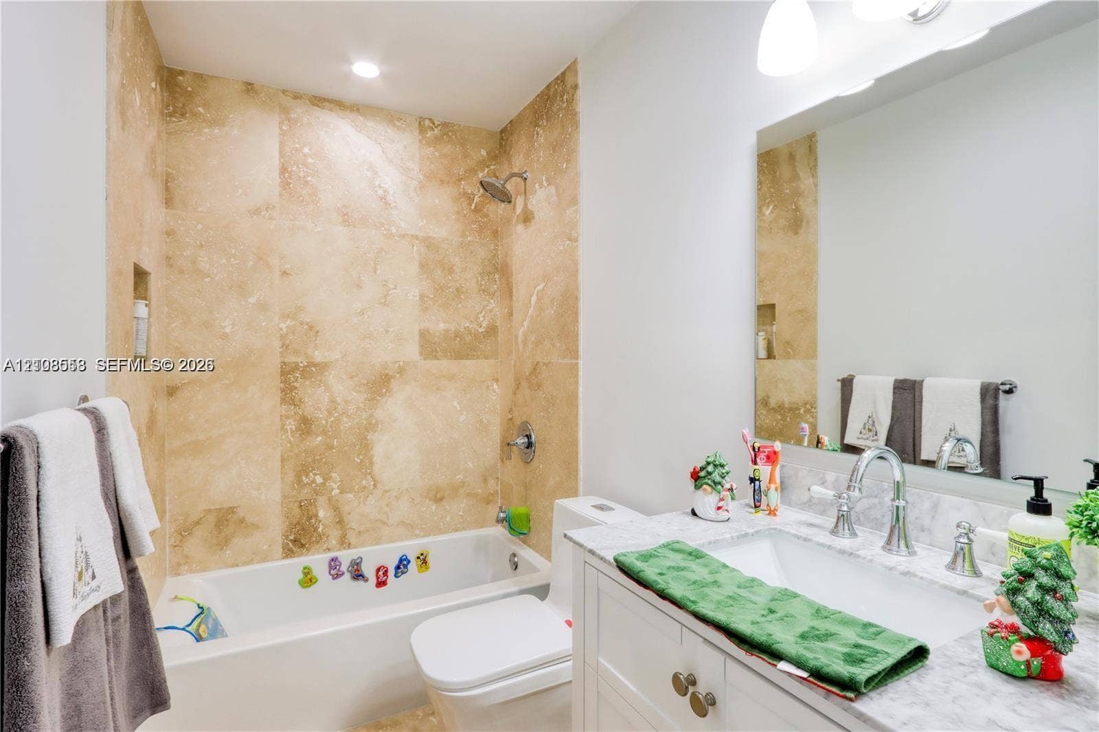 10478 SW 75th Lane, #10478, Miami, Miami, FL 33173 Bathroom featuring large-format natural stone wall tile, an undermount rectangular sink, a light-toned stone vanity countertop, white cabinetry with metallic hardware, and a large wall-mounted mirror