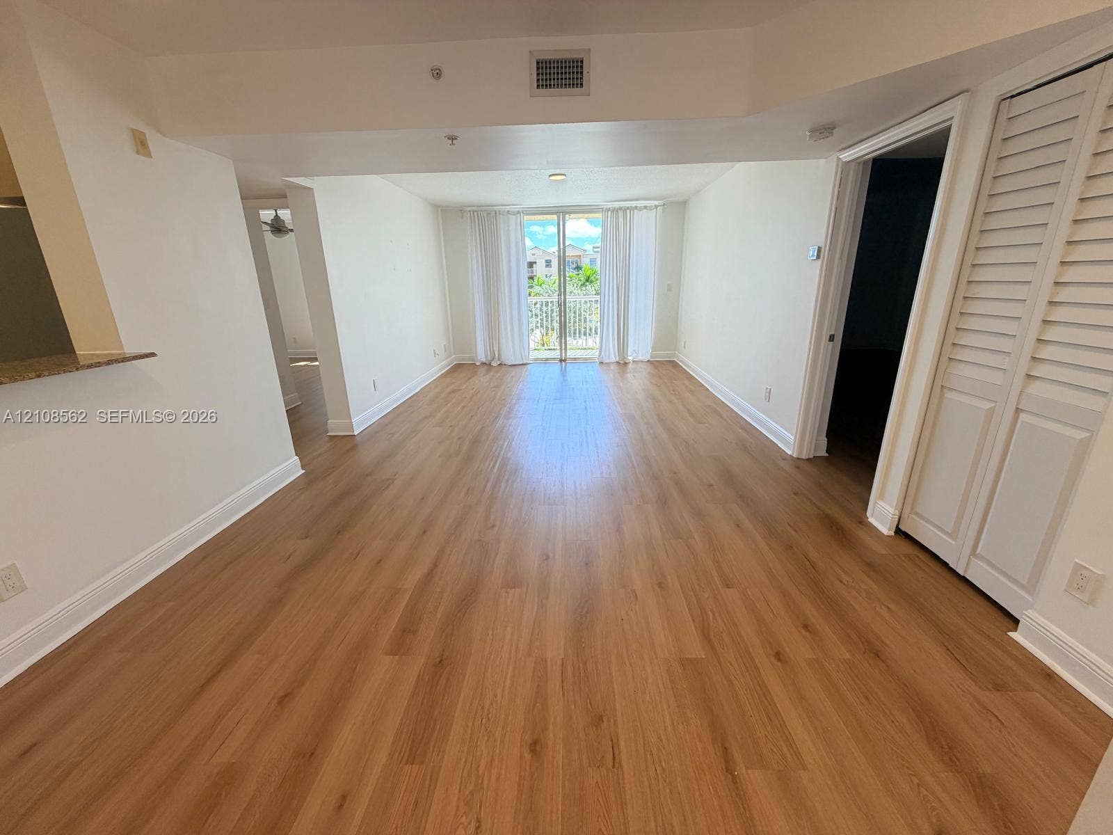 Open-concept interior featuring wood-finish flooring, louvered closet doors, and a glass-paneled sliding door opening to a balcony