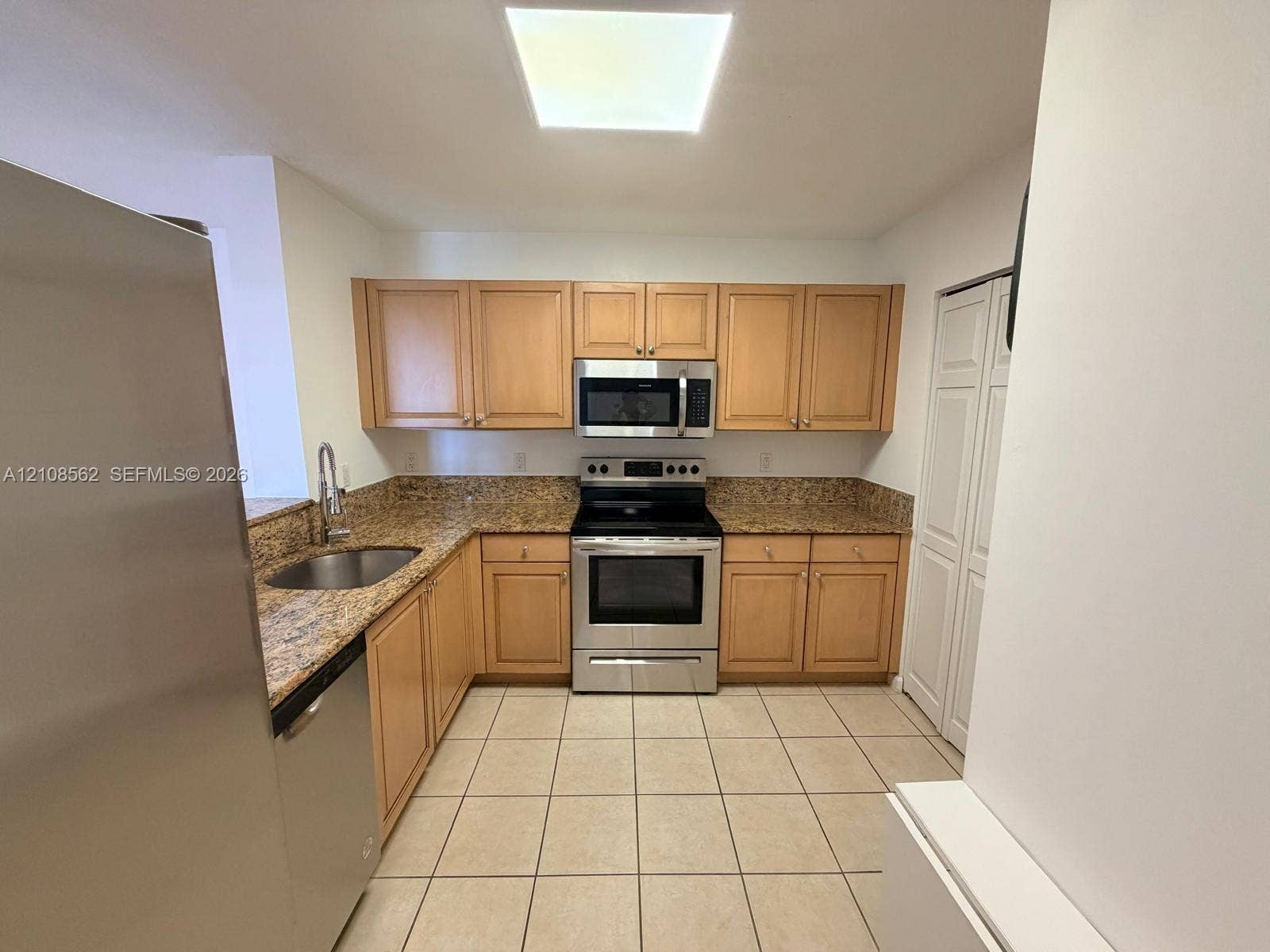 Kitchen featuring light wood cabinetry, stone-surface countertops, tile flooring, stainless steel appliances, and a recessed ceiling light