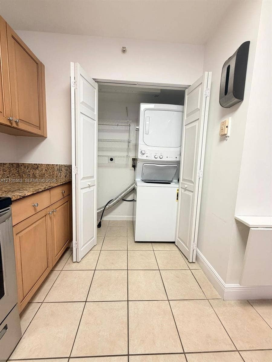 Laundry area featuring a stacked washer and dryer, tile flooring, built-in cabinetry, and stone-finish countertop