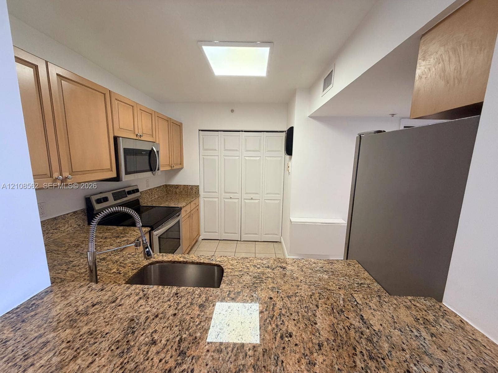 Kitchen featuring stone countertops, natural wood cabinetry, stainless steel appliances, a pull-down kitchen faucet, and bi-fold closet doors