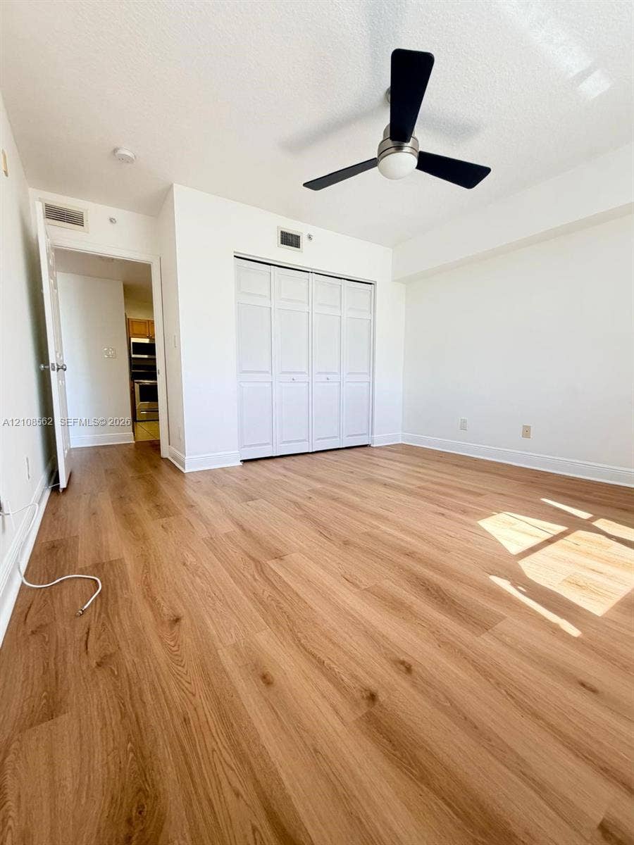 Room featuring wood-finish flooring, a ceiling fan with matte black blades, and a closet with bifold doors