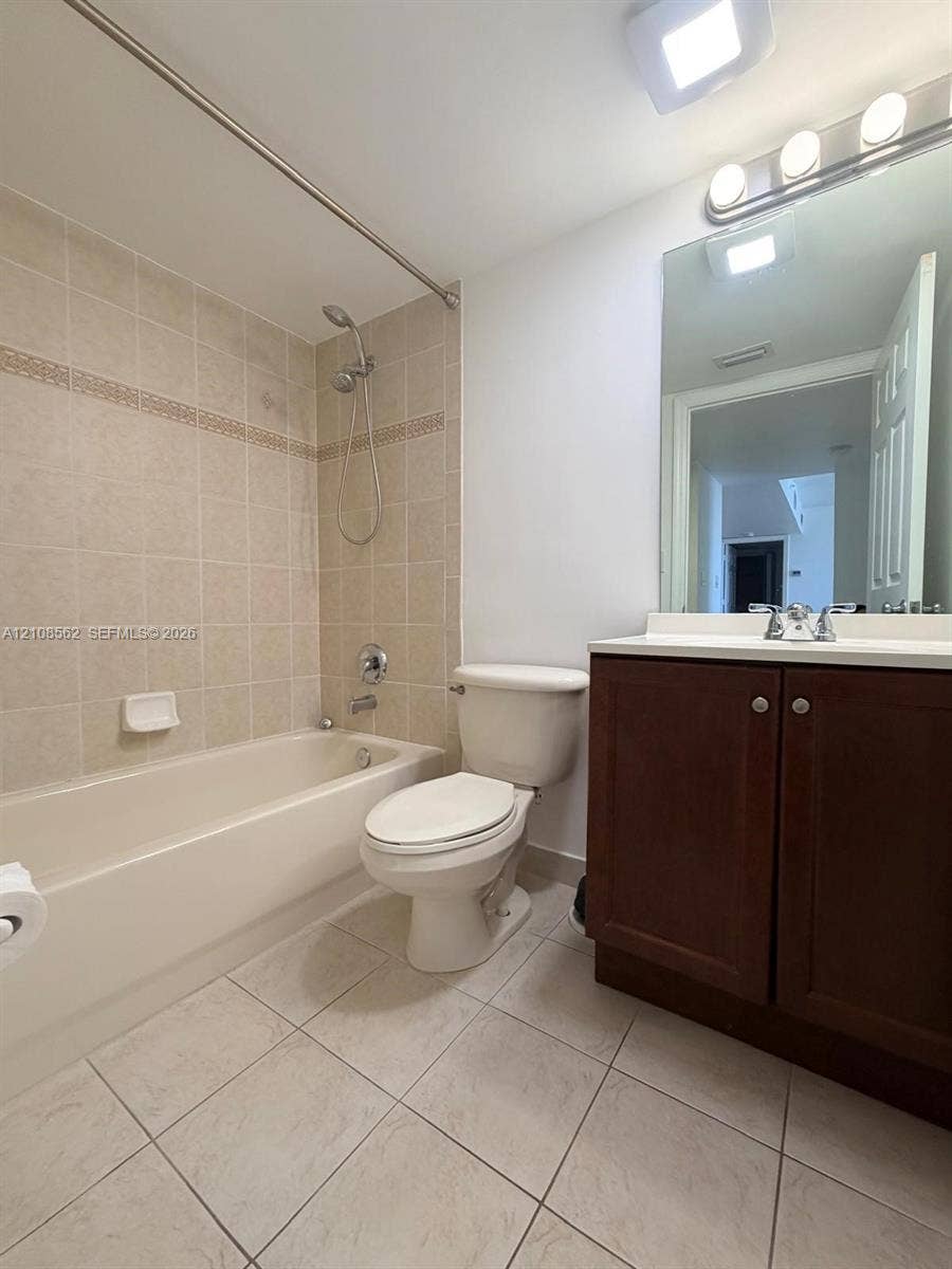 Bathroom featuring a tub-shower combination with ceramic tile surround, dark wood-finish cabinetry, a white countertop, and ceramic floor tiling