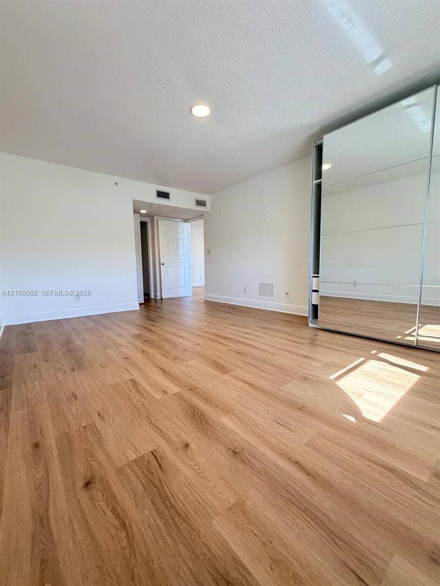 Wood-finish flooring, recessed ceiling lighting, and expansive floor-to-ceiling mirrored closet doors