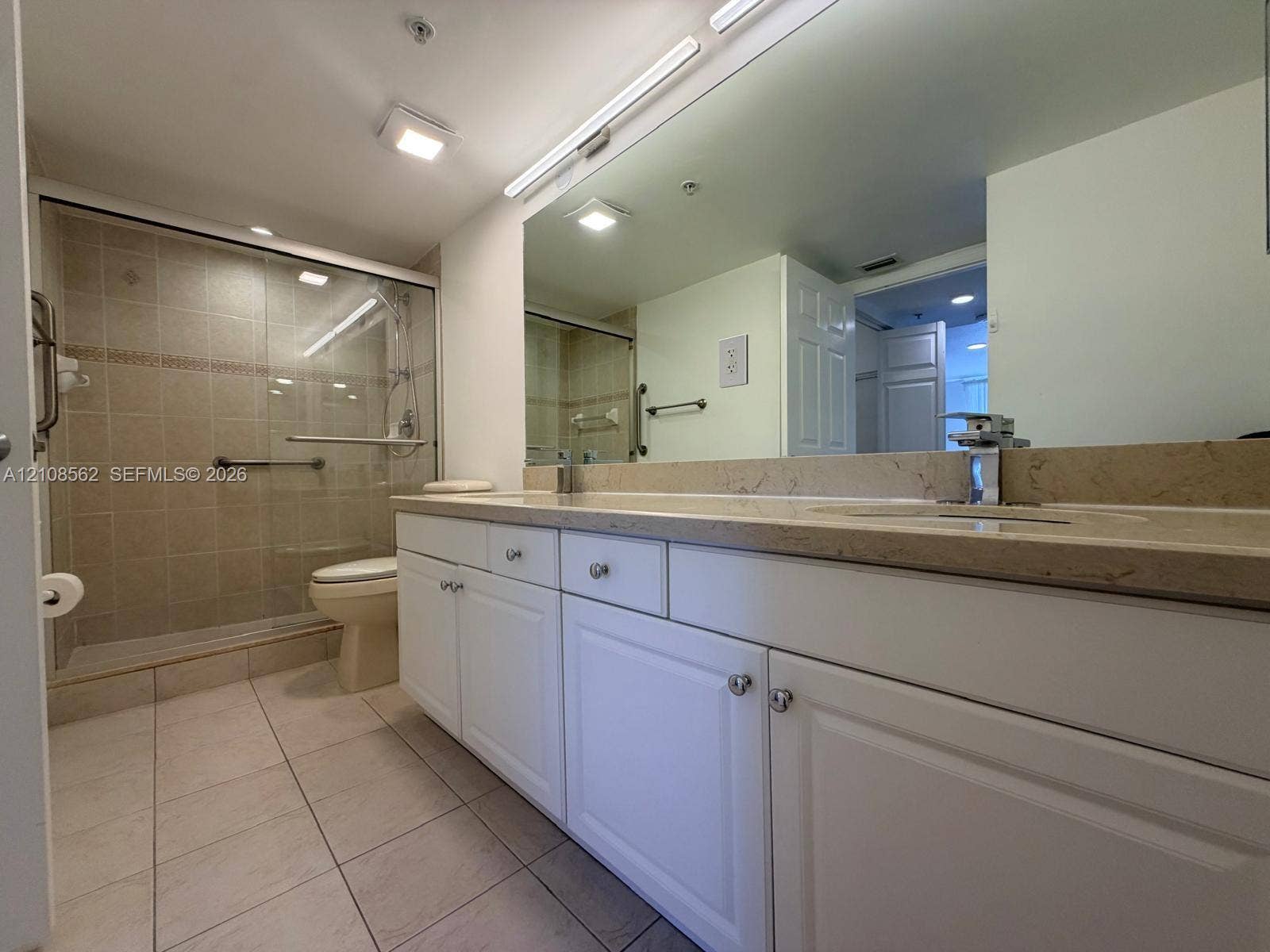 Bathroom featuring white cabinetry, stone-surface countertop, full-width wall mirror, and walk-in shower with glass enclosure
