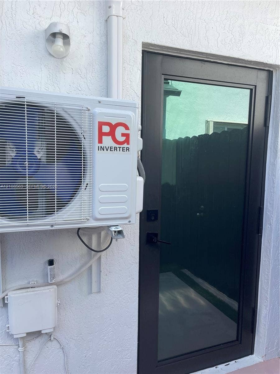 14554 SW 161 Court, #Studio, Miami, Miami, FL 33196 Exterior wall-mounted ductless inverter AC unit, black-framed glass entry door, and wall-mounted exterior light fixture