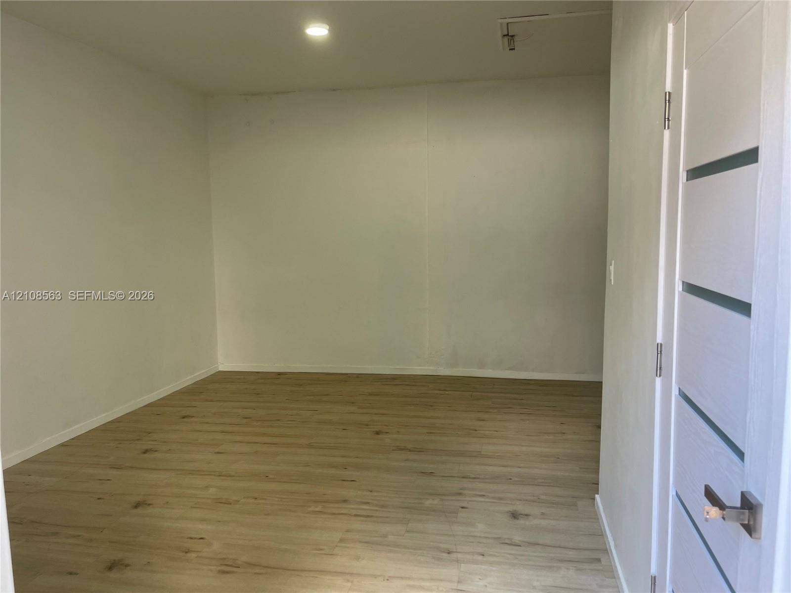 14554 SW 161 Court, #Studio, Miami, Miami, FL 33196 Neutral-toned interior room featuring wood-finish flooring, recessed lighting, and a modern five-panel horizontal door with a metallic handle