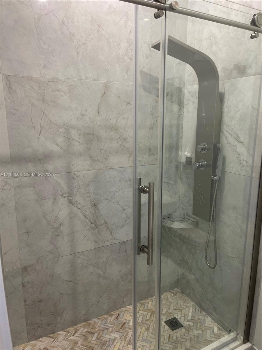 14554 SW 161 Court, #Studio, Miami, Miami, FL 33196 Walk-in shower featuring large-format stone-pattern wall tile, herringbone-pattern stone tile flooring, a glass sliding door with metal hardware, and a multi-function shower panel system