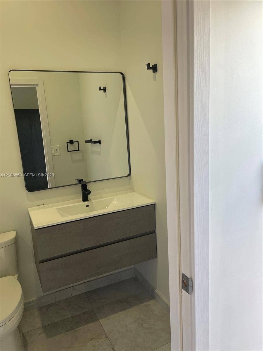 14554 SW 161 Court, #Studio, Miami, Miami, FL 33196 Floating dual-drawer vanity with a white integrated basin, matte black faucet, rectangular mirror with thin dark frame, and coordinating matte black wall-mounted hardware