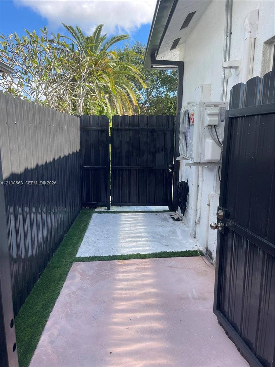 14554 SW 161 Court, #Studio, Miami, Miami, FL 33196 Side exterior space featuring privacy metal fencing, a gated entry, and a paved walkway bordered by synthetic turf