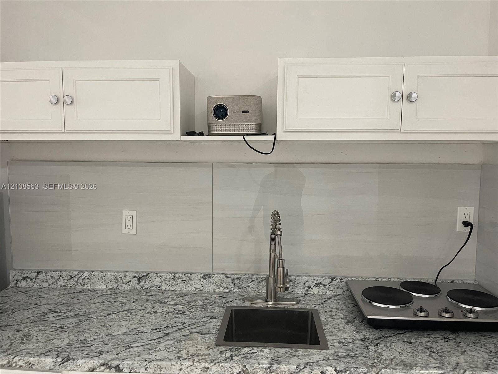 14554 SW 161 Court, #Studio, Miami, Miami, FL 33196 Kitchen area featuring stone-patterned countertops, a stainless steel undermount sink, a pull-down high-arch faucet, a smooth-top electric cooktop, and white cabinetry