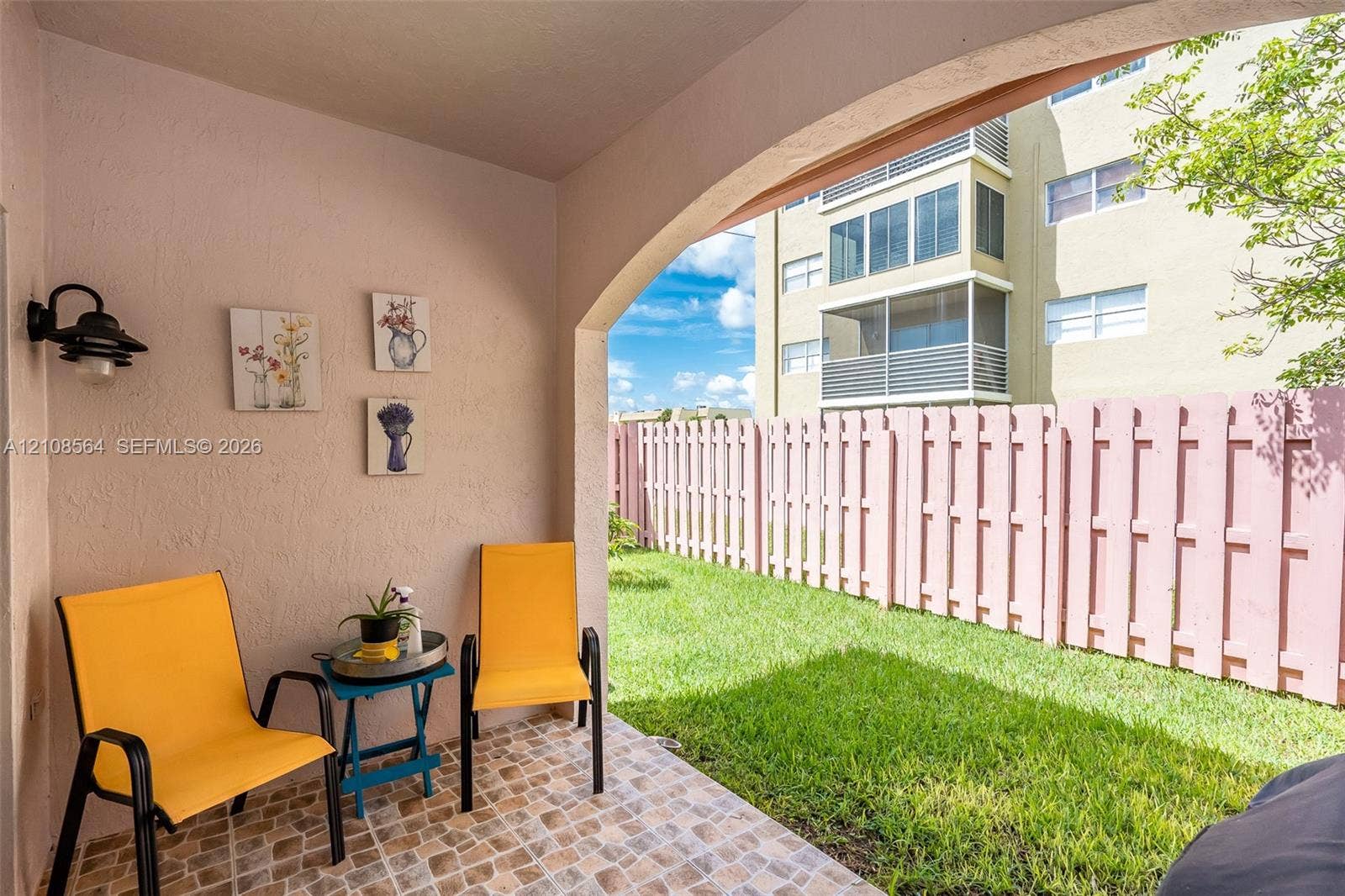 3111 NW 86th Avenue, Sunrise, FL 33351 Covered patio featuring an arched entryway, tile flooring, and wall-mounted exterior lighting, opening to a private lawn enclosed by a fence