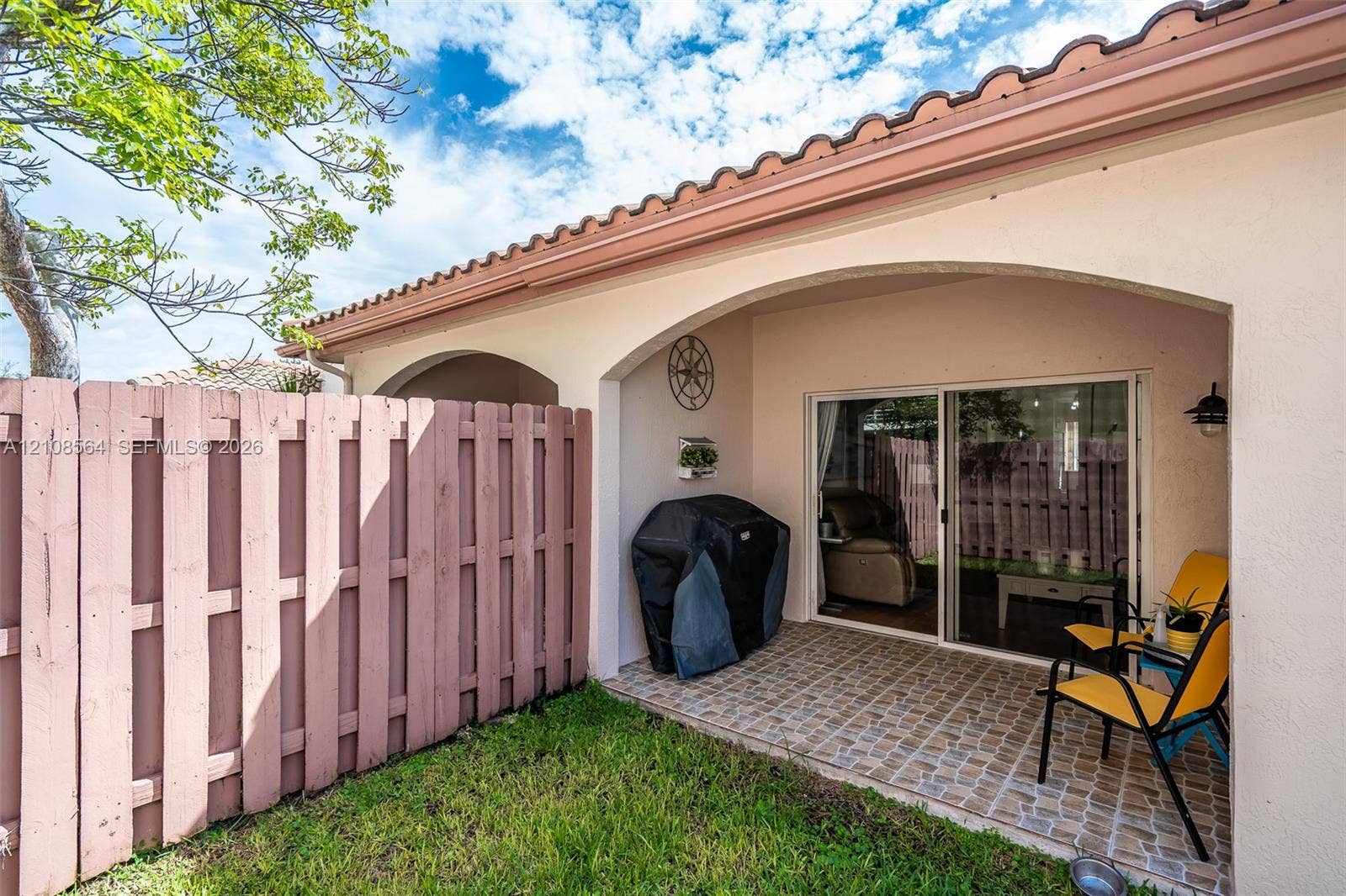 3111 NW 86th Avenue, Sunrise, FL 33351 Covered patio featuring stone-finish tile flooring and arched architectural detailing, enclosed by privacy fencing and sliding glass doors