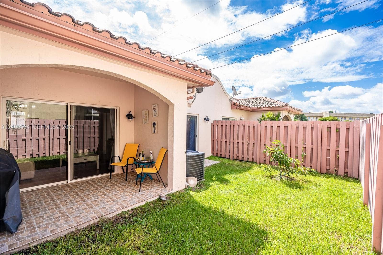 3111 NW 86th Avenue, Sunrise, FL 33351 Covered patio with tile flooring, sliding glass doors, and enclosed backyard featuring a privacy fence and manicured lawn