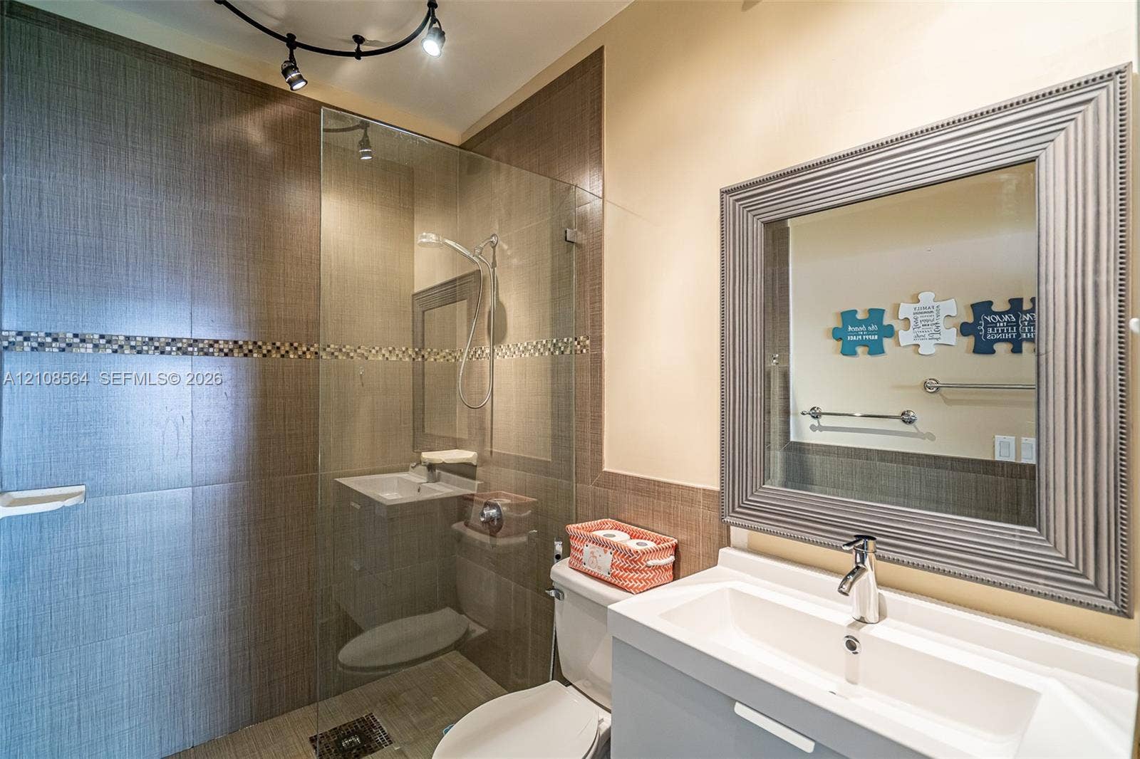 3111 NW 86th Avenue, Sunrise, FL 33351 Bathroom featuring a glass-enclosed walk-in shower with floor-to-ceiling textured tile, a decorative mosaic accent border, a floating vanity with a rectangular basin, and a framed mirror