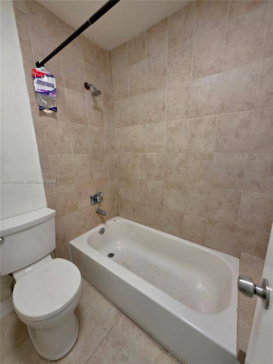 Full-sized bathtub with tile surround, porcelain toilet, and chrome-finished plumbing fixtures