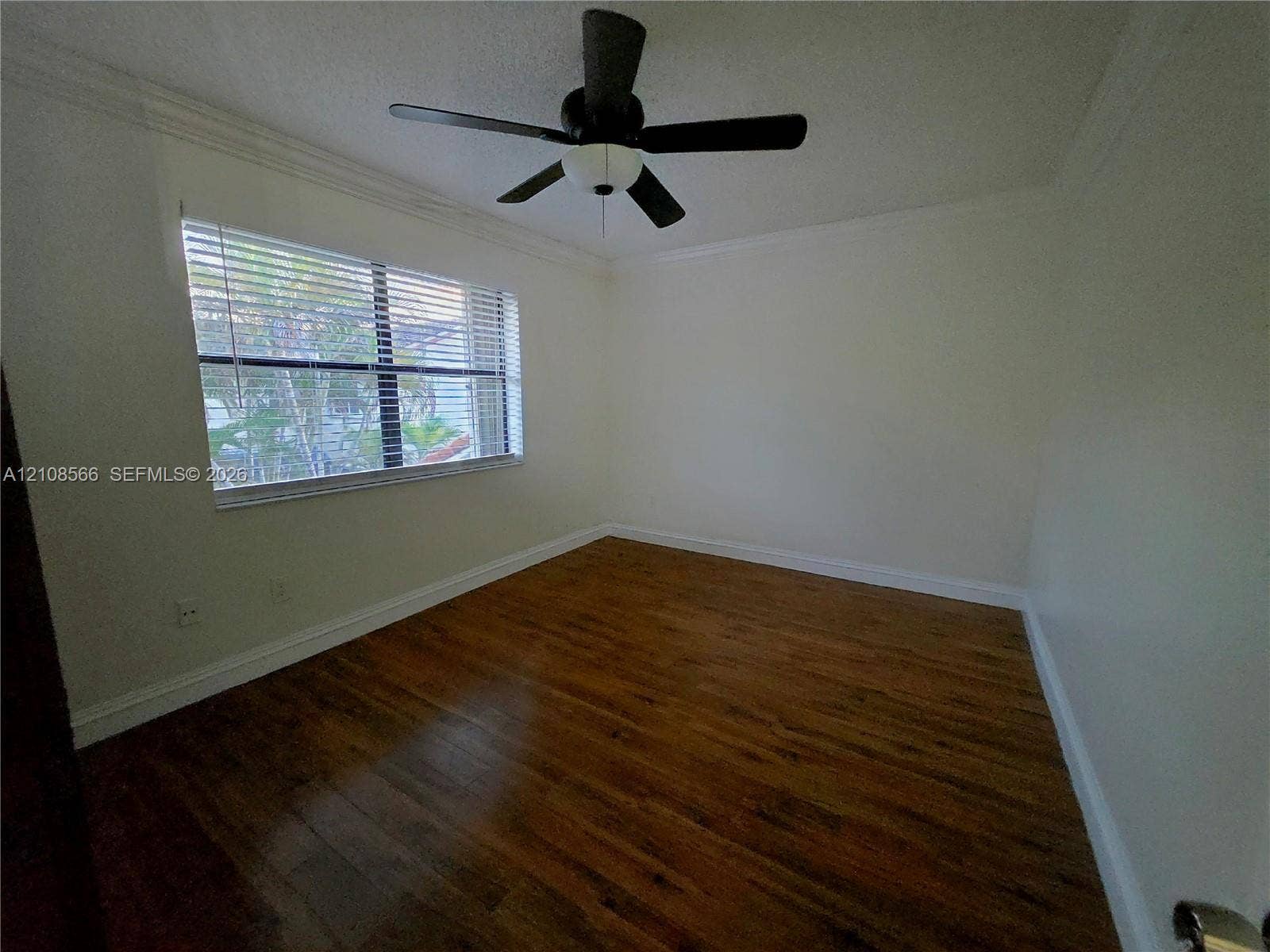 Room featuring wood-finish flooring, a multi-blade ceiling fan with integrated lighting, and a large window with horizontal blinds