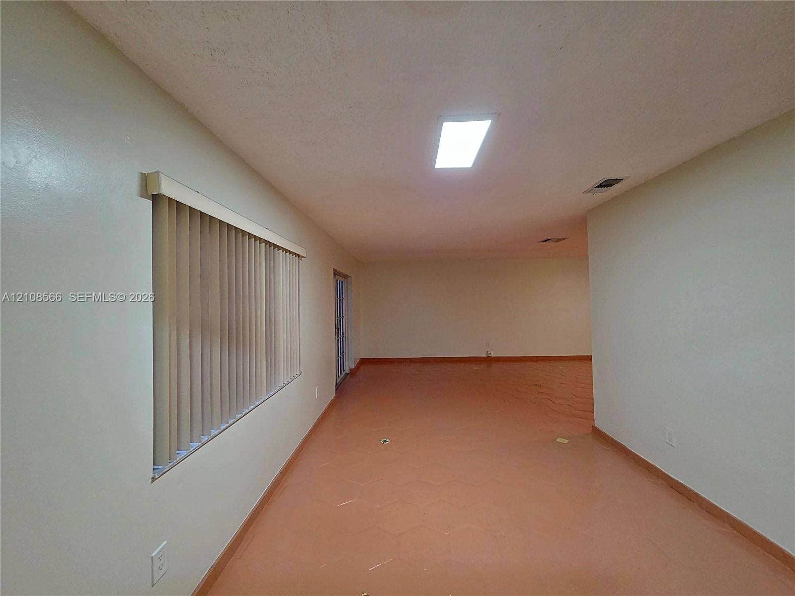 Neutral interior space featuring hexagonal tile flooring, vertical window blinds, and a recessed ceiling light fixture
