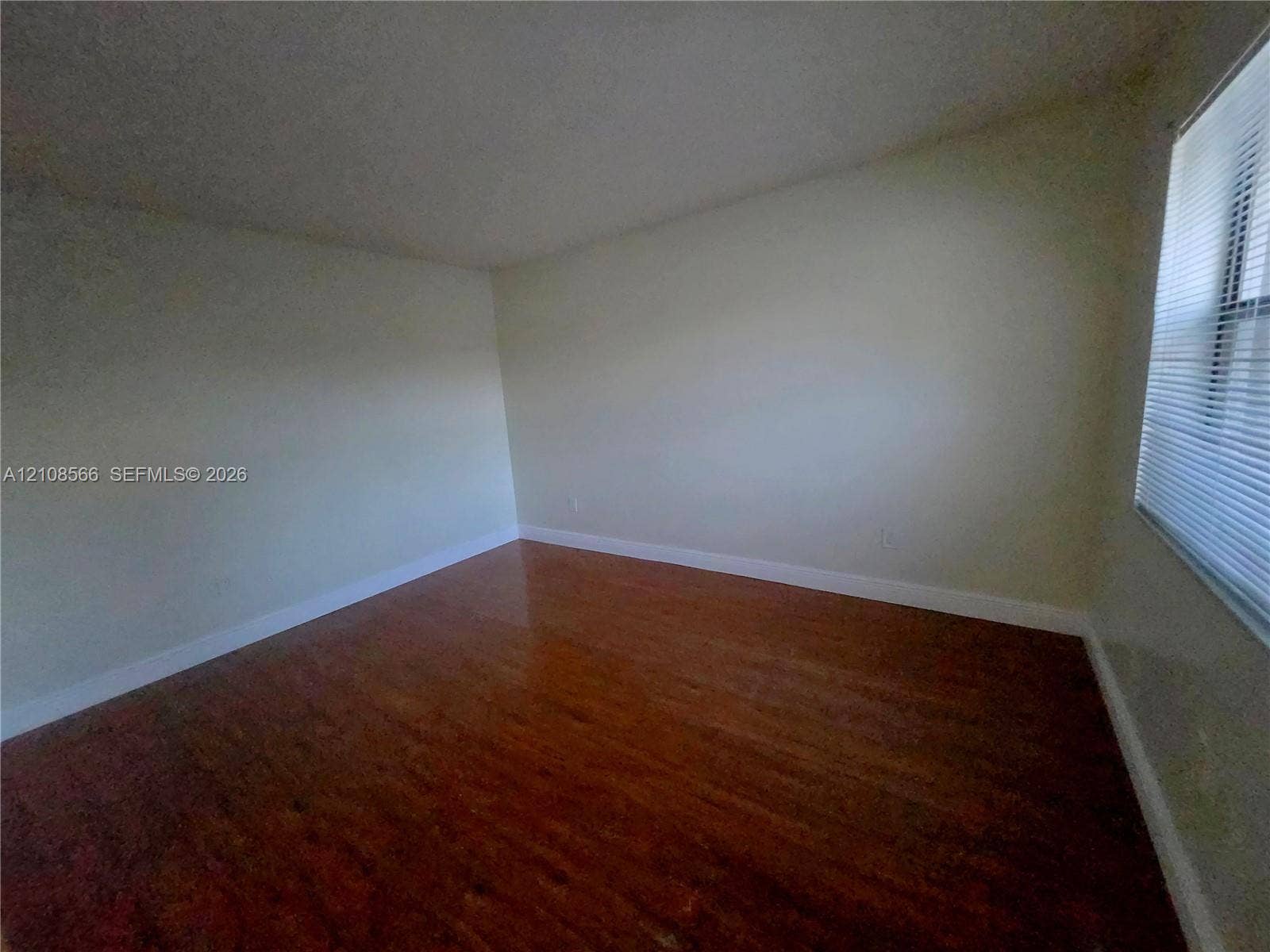 Room featuring wood-finish flooring and a window with horizontal blinds