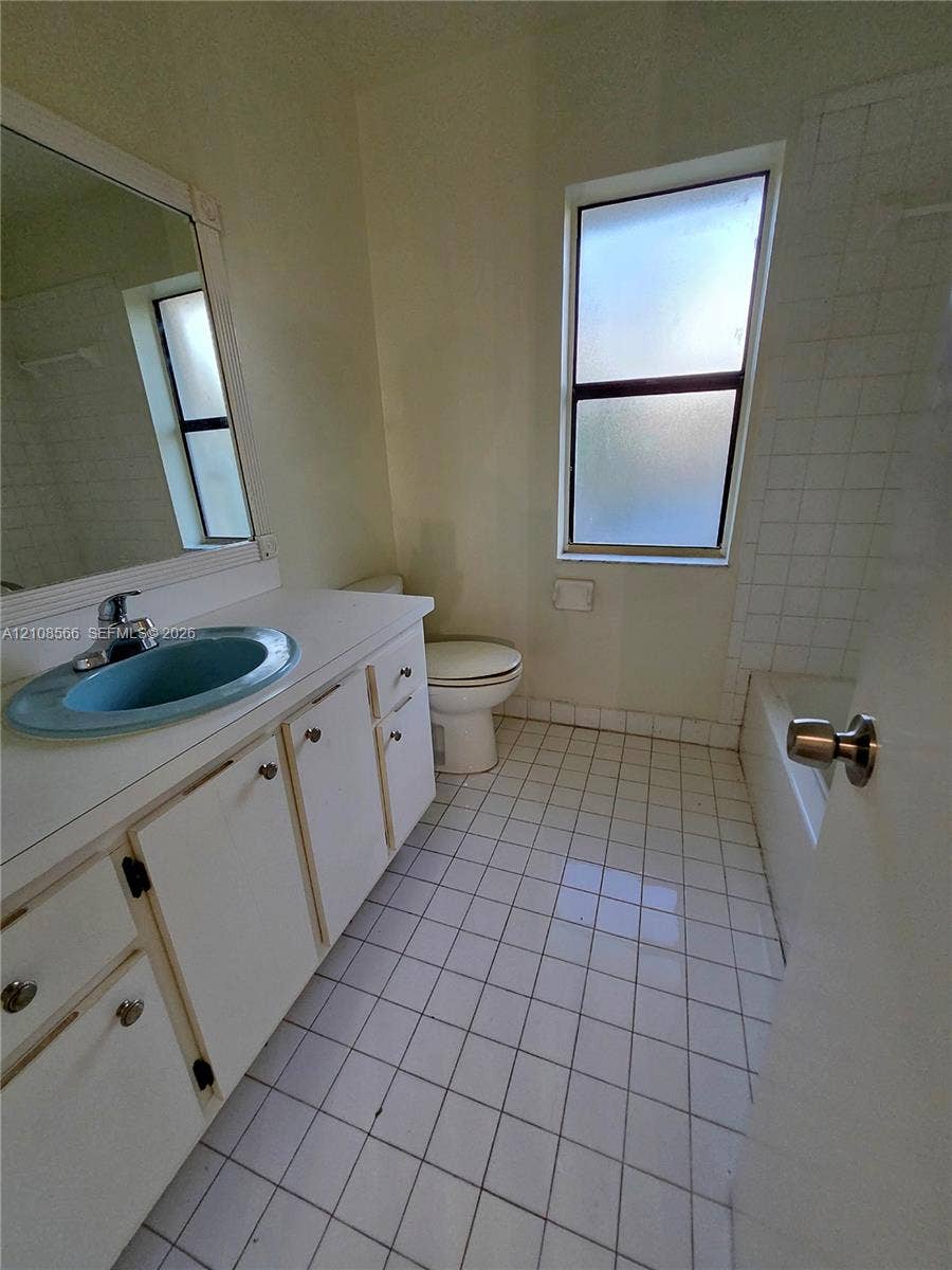 Bathroom featuring a white vanity cabinet, solid-surface countertop with an integrated blue oval sink, chrome-finish faucet, square tile flooring, and a shower-tub combination with tiled surround
