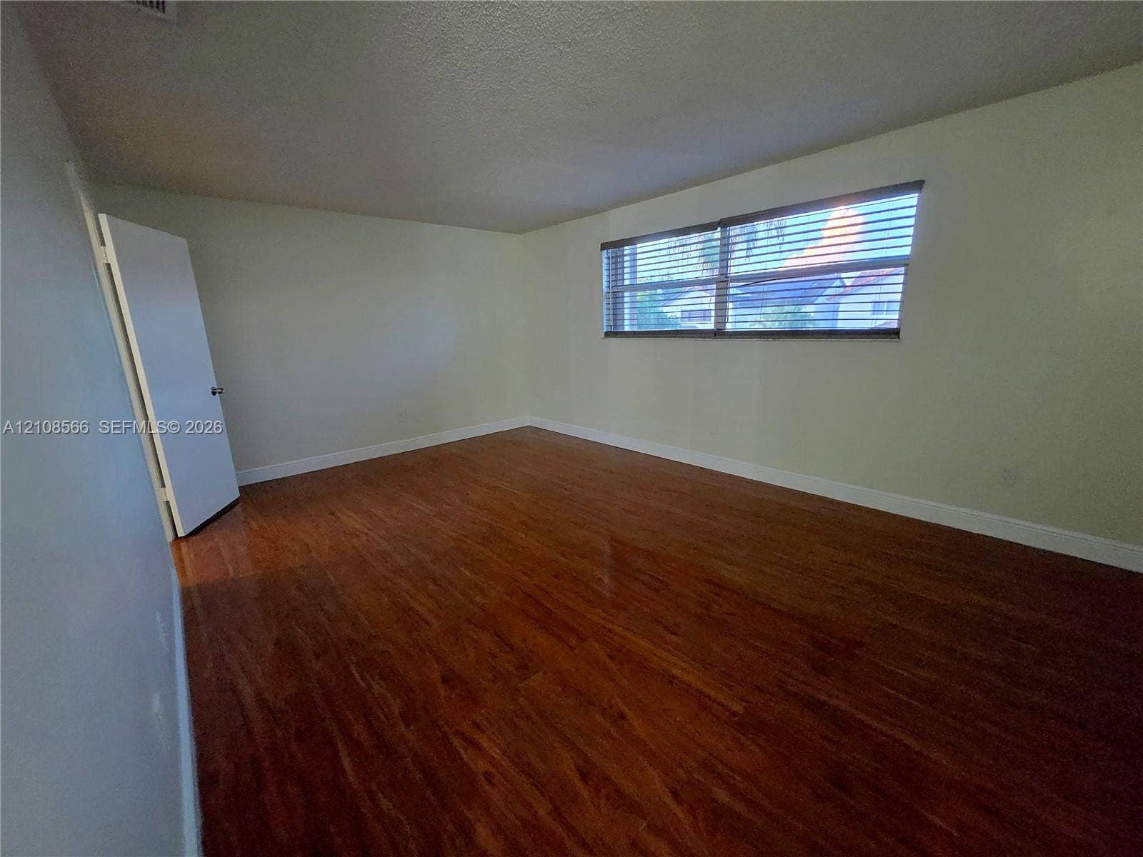 Interior space featuring wood-finish flooring, a horizontal window with installed blinds, and a solid-core door
