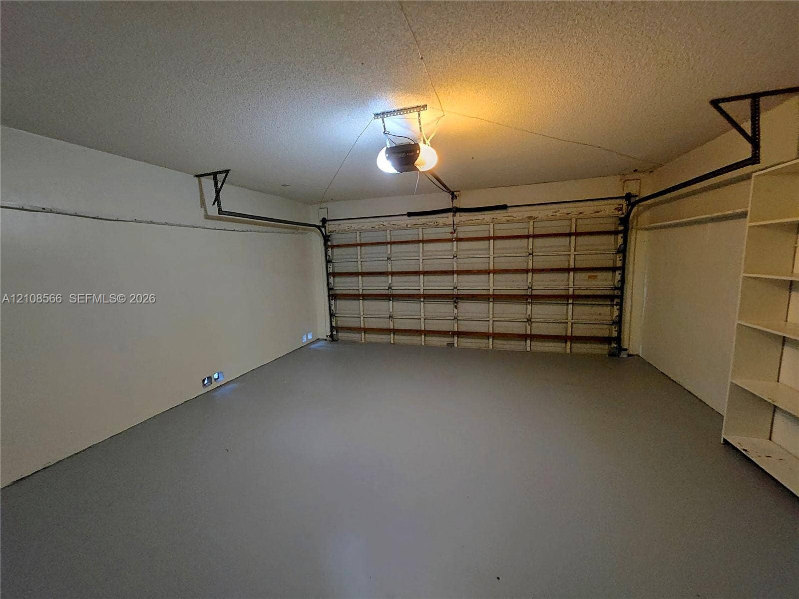 Enclosed garage featuring painted concrete flooring, a horizontal paneled overhead door, an automated door opener, and built-in shelving