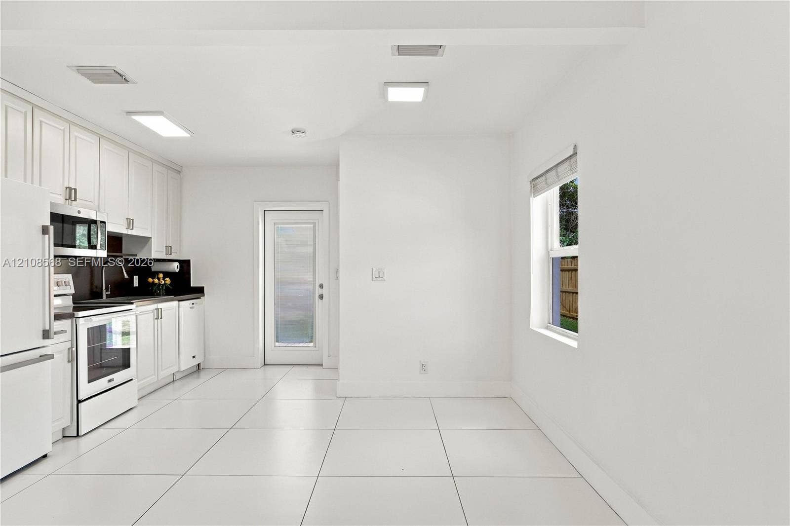 Kitchen featuring white shaker-style cabinetry, dark stone-finish countertops, tile flooring, and integrated white appliances