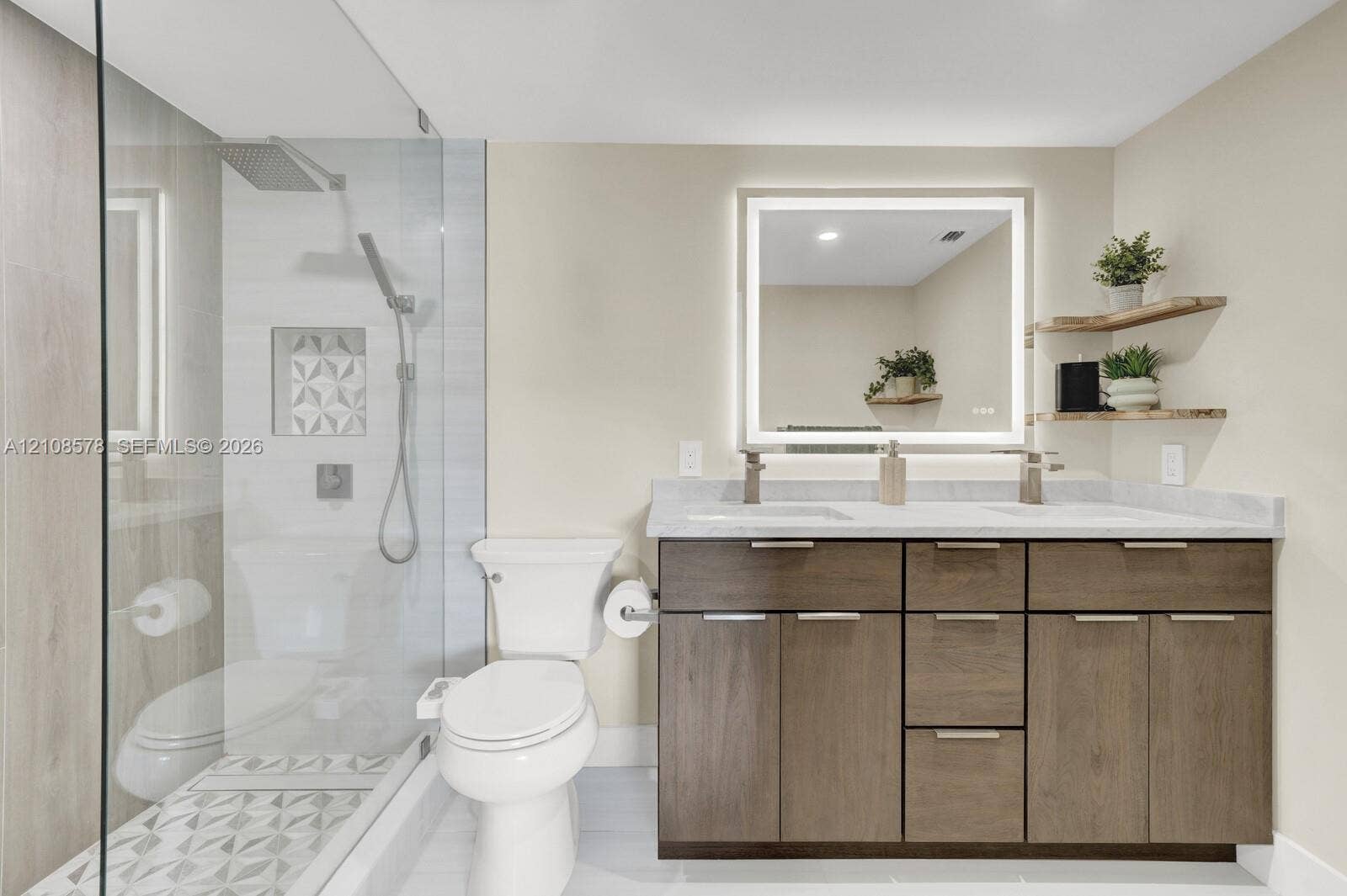 3005 Portofino Isle, #N2, Coconut Creek, Coconut Creek, FL 33066 Bathroom featuring a dual-sink vanity with wood-finish cabinetry, a backlit mirror, a glass-enclosed shower with patterned tile inlay, and floating wood-finished shelving
