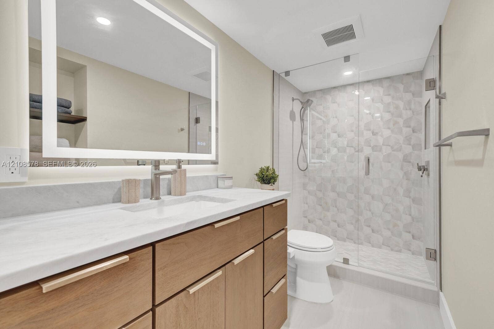 3005 Portofino Isle, #N2, Coconut Creek, Coconut Creek, FL 33066 Wood-finish vanity with a stone countertop, illuminated rectangular mirror, and a glass-enclosed walk-in shower featuring geometric tile accents
